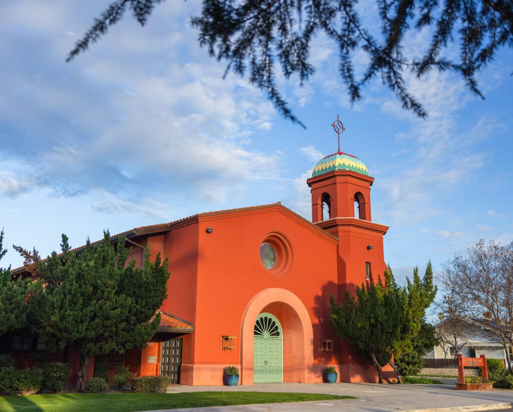 Front facade of the red church showing arched entrance, ornate tiled dome, bell tower, and ornamental details